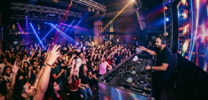 Energetic nightclub scene with a DJ performing for a large crowd under professional stage lighting